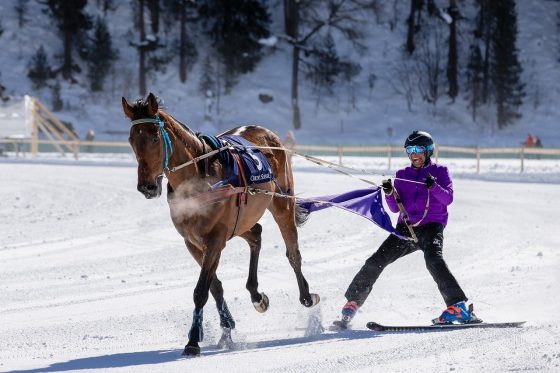Women skiing behind horse.